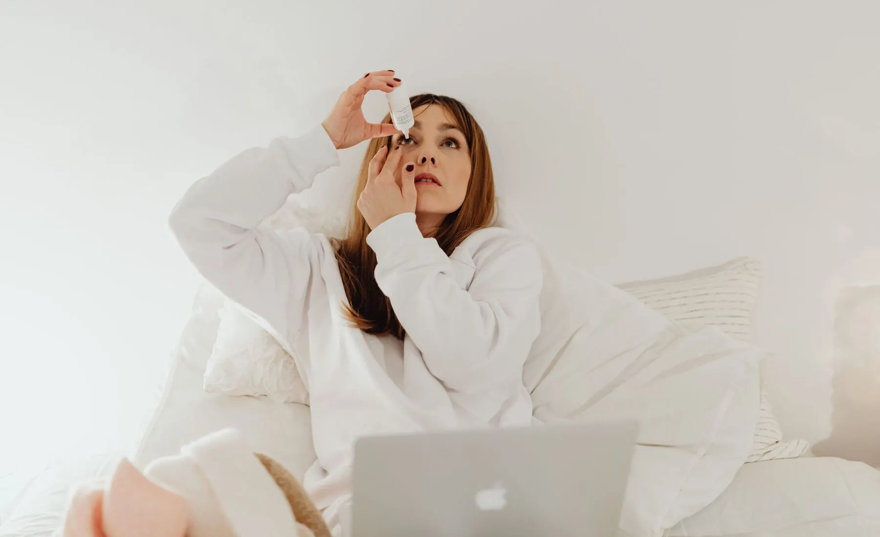 Woman applying lubricating eye drops while resting at home