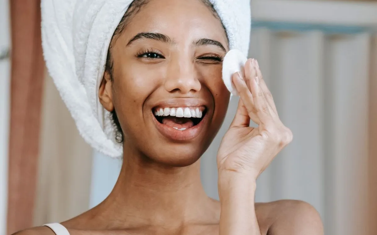 Smiling woman gently cleaning around her eye with a cotton pad